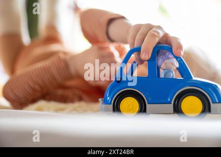 Bambino che gioca con un'auto giocattolo blu su una superficie morbida con un'attenzione particolare all'auto e al bambino sullo sfondo sfocato. Panc06142 Copyright: XConnectxIma Foto Stock