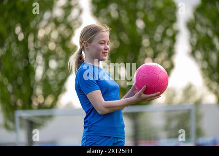 Giovane atleta sorridente che regge un pallone da calcio rosa su un campo con pali di porta sullo sfondo. Panc06281 Copyright: XConnectxImagesx Foto Stock