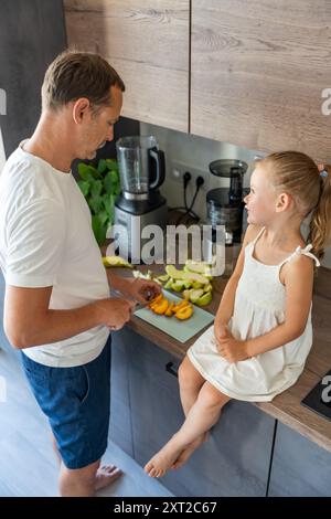 Famiglia con un giovane padre e la sua piccola figlia che preparano frutta per un succo sano o frullato in cucina Foto Stock