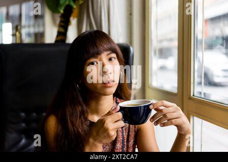 Giovane donna asiatica che beve caffè caldo rilasciato Foto Stock
