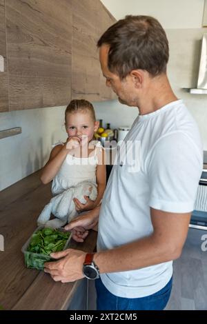 Famiglia con un giovane padre e la sua piccola figlia che preparano verdure per un succo o frullato sano in cucina Foto Stock