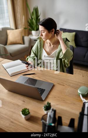 Una donna lavora in remoto alla scrivania di casa, utilizzando il computer portatile e il telefono. Foto Stock