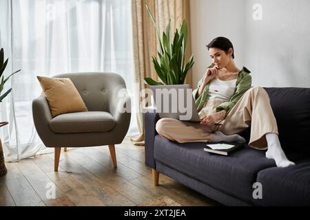 Una donna lavora in remoto da casa, guardando attentamente il suo notebook. Foto Stock