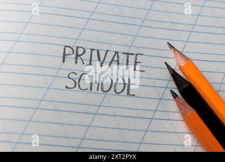 La scuola privata è scritta su un pezzo di carta con tre matite sopra. Le matite sono nere e arancioni, e sono disposte in modo che non siano Foto Stock