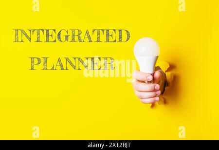 Una persona che tiene in mano una lampadina con le parole Integrated Planner riportate di seguito. L'immagine ha un'atmosfera luminosa e allegra, con sfondo giallo Foto Stock