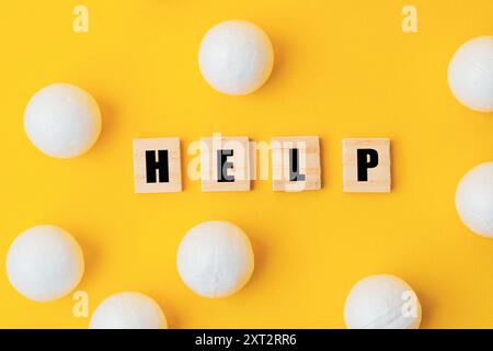 Uno sfondo giallo con un grande gruppo di palline bianche sparse intorno ad esso. La parola aiuto è scritta in lettere nere sopra le palle, creando una S. Foto Stock