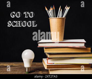 Una pila di libri e una lampadina su un tavolo con le parole Go to School scritte in gesso Foto Stock