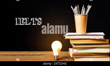 Una pila di libri con una lampadina sopra di loro e la parola IELTS scritta sul muro dietro di loro Foto Stock