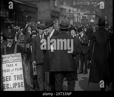 Uomini che indossano tavole sandwich "Pathe Gazette" che distribuiscono pezzi di pellicola Polaroid alla folla con cui vedere un'eclissi solare parziale, 1921. Da "Time to Remember - The Time When Little Happened", 1921 (Reel 2); eventi del 1921 - trattato irlandese, acrobazie pazze e giornali al lavoro. Foto Stock