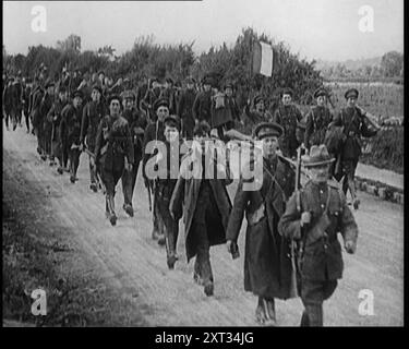 I soldati dello Stato libero irlandese che marciano lungo una strada, 1922. "Dopo anni di spargimento di sangue, fu firmato un trattato, e a Dublino, una nuova bandiera sostituì la bandiera dell'Unione. L'Irlanda, salvo le sei contee dell'Ulster, era diventata lo Stato libero d'Irlanda... lo Stato libero formò immediatamente il proprio esercito... migliaia si precipitarono ad arruolarsi. Era patriottico, ed era un lavoro... l'entusiasmo compensava la mancanza iniziale di attrezzature. Ed era un po' ironico che questi primi soldati di un'Irlanda libera indossassero il cachi britannico, tinti di verde. L'Irlanda del Sud era libera, e l'Irlanda si rallegrava”. Da "tempo per ricordare - seduto fermo e G Foto Stock