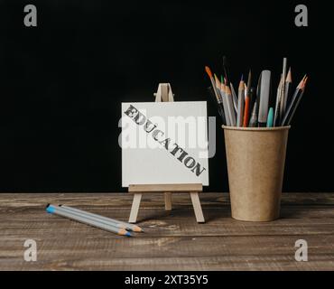 Una lavagna bianca con la parola "educazione". Un piedistallo in legno che regge una lavagna bianca e una tazza di matite Foto Stock