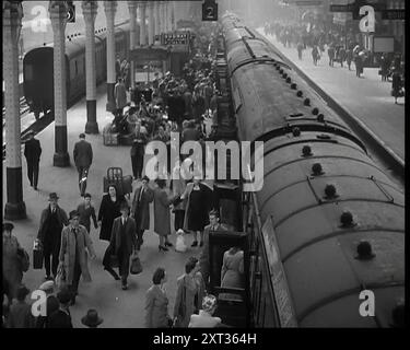 Guardando in basso lungo un binario dei treni con i passeggeri che camminano lungo, che si imbarcano e sbarcano, seduti su pile di bagagli, con i bagagli in attesa sui tram, un chiosco e un ingresso della metropolitana possono essere visti sullo sfondo, 1938. Da "Time to Remember - Wind Up Week", 1938 (Reel 2); documentario sul 1938 - le persone diventano consapevoli della crescente minaccia della guerra. Foto Stock