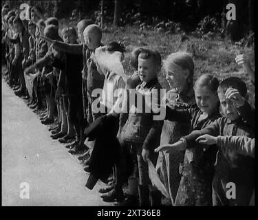 Bambini tedeschi in piedi al fianco di una nuova strada, alcuni di loro alzano le armi in una salute nazista, 1937. "La prima delle nuove autobahn di [Hitler] era stata aperta, e chi doveva rendersi conto allora che il loro vero scopo era il trasporto veloce delle truppe". Da "Time to Remember - Sense of Values", 1937 (Reel 3); documentario sugli eventi del 1937, guerra in Estremo Oriente, costruire fino alla guerra in Europa. Foto Stock