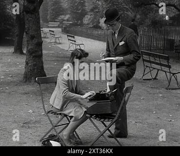 Un uomo e una donna che prendono appunti in un parco, 1941. La Gran Bretagna durante la seconda guerra mondiale. La Gran Bretagna, all'inizio del 1941, non aveva sentito parlare dell'operazione Barbarossa. Ma sapeva tutto della guerra con la Germania nazista. Ormai era abbastanza abituata ai tag "business as usual", l'improvvisazione, il making-do...it era incredibile quanto fosse ancora vivo, attivo e funzionante. Da "Time to Remember - Operation Barbarossa", 1941 (Reel 1); documentario sugli eventi del 1941, sul fronte orientale e a Pearl Harbour. Foto Stock