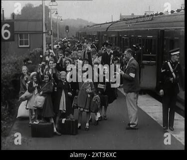 Sfollati britannici maschi e femmine sul binario di una piccola stazione nella campagna britannica con il treno in piedi con le sue porte aperte, 1939. Da "Time to Remember - The Reluctant Warriors", 1939 ( Reel 3); documentario sugli eventi del 1939 - i preparativi per la guerra e poi scoppiano le ostilità. Foto Stock