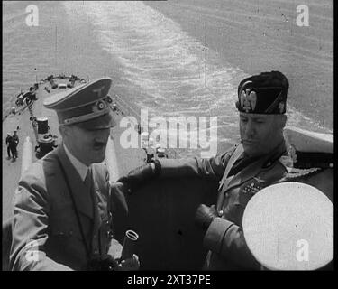 Adolf Hitler, il leader tedesco, a bordo di una nave da guerra della Marina italiana in una revisione navale con il leader italiano, Benito Mussolini, nel Golfo di Napoli, 1937. "Sul ponte di una nave da battaglia nel Mediterraneo, il leader di tutti i tedeschi è intrattenuto dal leader di tutti gli italiani, (e non intendiamo il re d'Italia). I ragazzi erano tutti lì insieme, ispezionando la flotta italiana e stimando la sua potenza di combattimento in caso ci fossero... problemi. From Time to Remember - Sense of Values, 1937 (Reel 1); documentario sugli eventi del 1937, War in the far East, Build Up Foto Stock