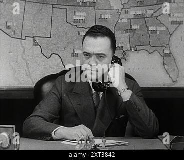 J. Edgar Hoover dell'FBI al telefono, 1942. Seconda guerra mondiale. "Per salvaguardare [i produttori statunitensi di armamenti e veicoli] da sabotatori e agenti, Hoover dell'FBI ha preso un bel po' di soldi in rete. Ci sono stati alcuni esperimenti sensazionali su agenti sospetti con prove sensazionali. Da Time to Remember - The End of the Beginning, 1942 (Reel 3); film documentario sugli eventi del 1942 e l'entrata in guerra dell'America. Foto Stock