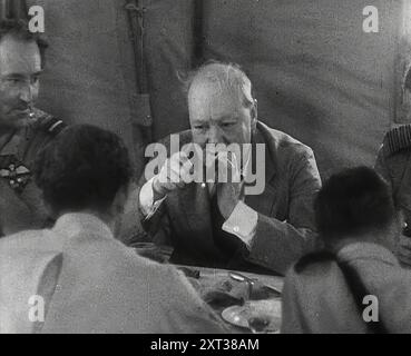 Winston Churchill con le truppe britanniche nel deserto, 1942. Seconda guerra mondiale. Il primo ministro britannico accende un sigaro in Nord Africa. "...lì in una tenda dietro le linee c'era il grande sigaro stesso, che rompeva il suo viaggio a Mosca per rimediare alle cose in Egitto". Da Time to Remember - The End of the Beginning, 1942 (Reel 3); film documentario sugli eventi del 1942 e l'entrata in guerra dell'America. Foto Stock