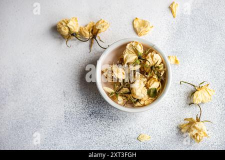 Vista ravvicinata delle rose appassite in una ciotola, elegantemente allestita su uno sfondo grigio testurizzato, i fiori secchi trasmettono un senso di bellezza senza tempo Foto Stock