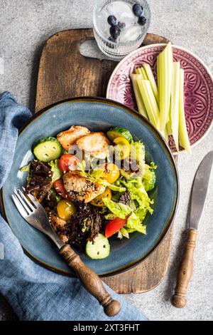 Vista dall'alto di una nutriente insalata fatta in casa con verdure fresche come lattuga, pomodori ciliegini, cetrioli e peperoni, accompagnate da un barbecue Foto Stock