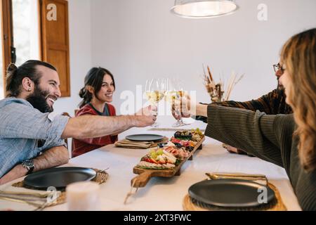 Due donne e due uomini brindano con bicchieri da vino a un tavolo ben allestito. Tutti sorridono e si impegnano nel momento facendo un contatto visivo con ciascuno di essi Foto Stock