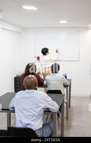 Insegnante che comunica con gli studenti adulti durante una lezione presso un'accademia di inglese, creando un ambiente di apprendimento collaborativo come scrive sul whi Foto Stock