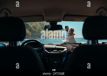 Guarda dall'interno di un'auto dove una coppia abbraccia affettuosamente l'oceano e le scogliere di Sao Miguel, Azzorre come sfondo. Foto Stock