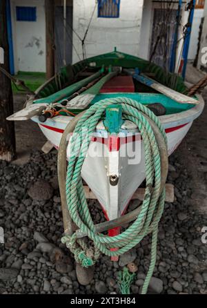 Una tradizionale barca da pesca dai colori vivaci del rosso, del verde e del bianco, poggia su una costa rocciosa, circondata da rustici attrezzi da pesca e ciottoli. Foto Stock