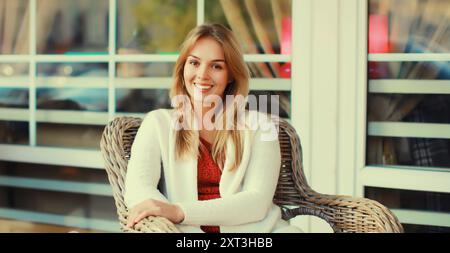 Ritratto di una bella donna bionda sorridente seduta su una sedia che aspetta nel caffè della città Foto Stock