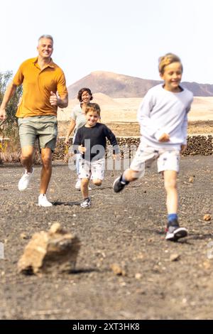 Famiglia con due ragazzi e i loro genitori che corrono gioiosamente in un parco con un'espressione gioiosa. Questo cattura un momento di divertimento e di legame con la famiglia Foto Stock
