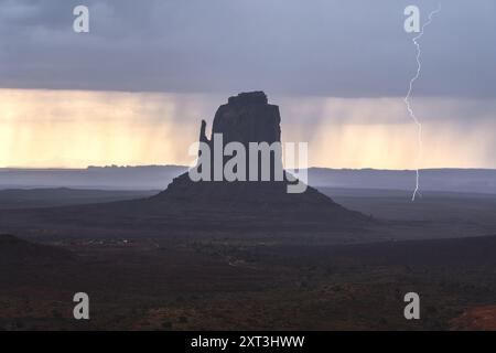 Un fulmine colpisce accanto a una torreggiante butte nella Monument Valley sotto nuvole buie e minacciose di tempesta, evidenziando la dura bellezza di questo paesaggio desertico Foto Stock