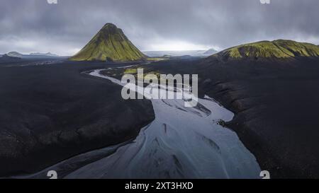 Ripresa aerea dell'impressionante vulcano Maelifell circondato da sabbie vulcaniche scure contrastate da un tortuoso fiume argenteo nelle remote Highlands di Icela Foto Stock