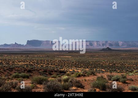 Immagine suggestiva della Monument Valley sotto un cielo scuro, che suggerisce una tempesta imminente, con vaste pianure aride e iconiche arenarie Foto Stock