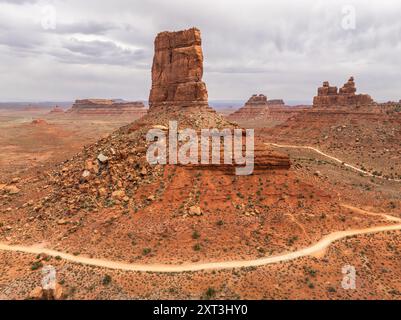 Uno scatto aereo mozzafiato che cattura una formazione rocciosa torreggiante nella Valle degli dei dello Utah, con vasti paesaggi aridi e tortuose strade sterrate sotto ov Foto Stock