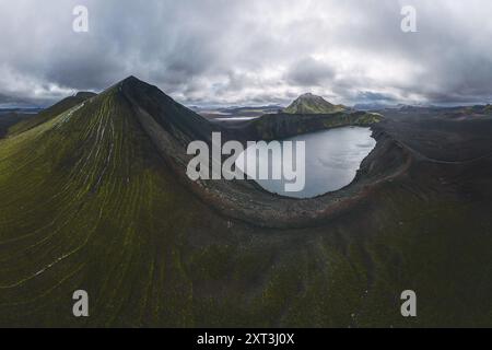 Incredibile ripresa aerea che cattura le montagne nere e verdi che circondano un tranquillo lago nelle Highlands dell'Islanda, sotto un cielo coperto Foto Stock