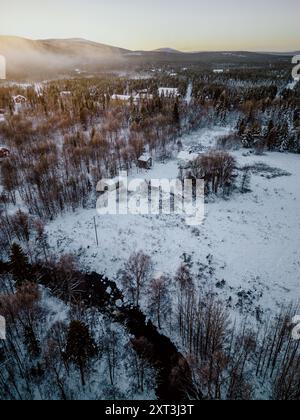 Accattivante fotografia aerea che mostra la serena bellezza di un paesaggio drappeggiato di neve in Lapponia, con boschi sparsi e un fiume serpeggiante in mezzo Foto Stock