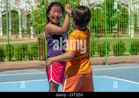 Due bambini sorridenti si impegnano in un allegro high-five su un colorato campo sportivo, sottolineando temi di amicizia e sana attività fisica in un mulo Foto Stock