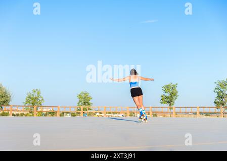 Una giovane donna gode di una giornata di sole, pattina con grazia su pattini in uno spazioso parco di pattinaggio all'aperto, dimostrando equilibrio e fiducia nella sua Foto Stock