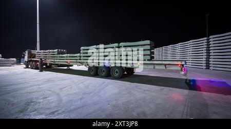 Un autocarro carico di traversine ferroviarie verniciate di verde parcheggiate di notte, in attesa del trasporto per l'uso in progetti di interior design. Foto Stock
