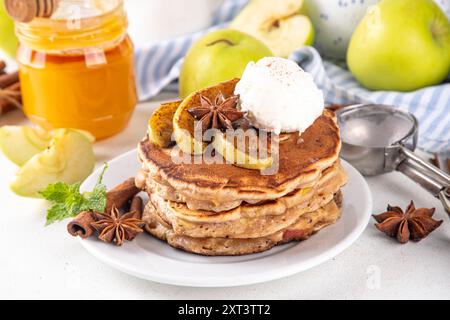 Dolci pancake autunnali con torta di mele piene di gelato e mele caramellate sulla parte superiore, tavolo da cucina con spezie, mele e barattolo di miele, copia spazio Foto Stock