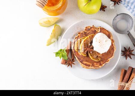 Dolci pancake autunnali con torta di mele piene di gelato e mele caramellate sulla parte superiore, tavolo da cucina con spezie, mele e barattolo di miele, copia spazio Foto Stock