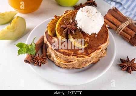 Dolci pancake autunnali con torta di mele piene di gelato e mele caramellate sulla parte superiore, tavolo da cucina con spezie, mele e barattolo di miele, copia spazio Foto Stock