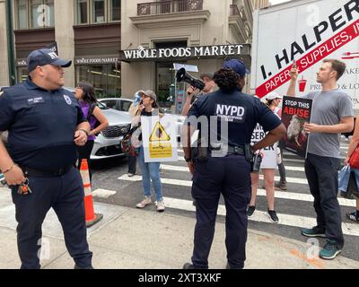 Membri del NYPD corral manifestanti per i diritti degli animali fuori dal negozio Crumbl a Chelsea a New York venerdì 9 agosto 2024 durante un'attivazione del marchio. I manifestanti si sono opposti alla catena dei biscotti che utilizza uova di galline tenute in presunte condizioni non sanitarie e abusive. (© Frances M. Roberts) Foto Stock