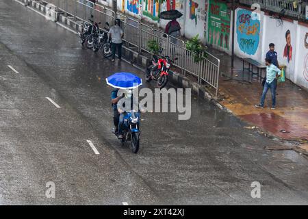 Dacca, Bangladesh. 13 agosto 2024. Un motociclista viaggia con un passeggero in possesso di un ombrello durante una giornata di pioggia. visto andare in giro per strada in una giornata di pioggia. La caduta dei monsoni ha rallentato il viaggio. (Foto di Sazzad Hossain/SOPA Images/Sipa USA) credito: SIPA USA/Alamy Live News Foto Stock