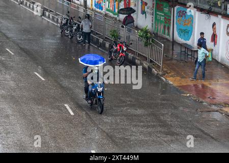 Dacca, Bangladesh. 13 agosto 2024. Un motociclista viaggia con un passeggero in possesso di un ombrello durante una giornata di pioggia. visto andare in giro per strada in una giornata di pioggia. Il downpour monsonico ha rallentato il viaggio (immagine di credito: © Sazzad Hossain/SOPA Images via ZUMA Press Wire) SOLO PER L'USO EDITORIALE! Non per USO commerciale! Foto Stock