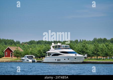 Moderno yacht a motore attraccato nel porto marittimo nel porticciolo durante il sole del giorno estivo. Grande yacht bianco ormeggiato su un molo. Concetto di svago estivo. Foto Stock