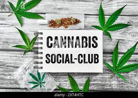 13 agosto 2024: Foglie di canapa con un giunto intorno a un blocco note con l'iscrizione: Cannabis Social Club. FOTOMONTAGGIO *** Hanfblätter mit einem Joint um ein Notizblock mit der Aufschrift: Cannabis Social-Club. FOTOMONTAGE Foto Stock