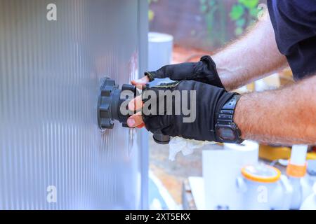 Un dipendente di un'azienda di manutenzione installa un sistema di clorazione per piscine e un sistema di filtraggio dell'acqua Foto Stock