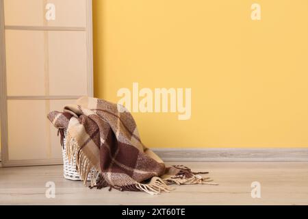 Cestino con nuova coperta morbida e schermo pieghevole vicino alla parete gialla in camera Foto Stock