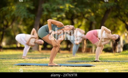 Lezione di yoga le ragazze eseguono Parivritta Uttanasana nel parco Foto Stock